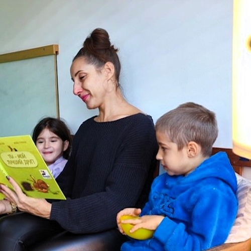 Halyna liest einem Jungen und einem Mädchen eine Geschichte auf Russisch vor. Die Kinder hören aufmerksam zu.