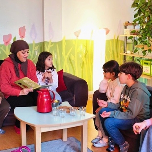 Kinder und eine Mutter hören gespannt einer arabischen Vorlesegeschichte zu. Auf dem Tisch stehen Tee und Gebäck bereit.