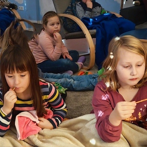 Kinder sitzen aufmerksam auf Decken und Kissen, hören gebannt einer Vorlesegeschichte zu.