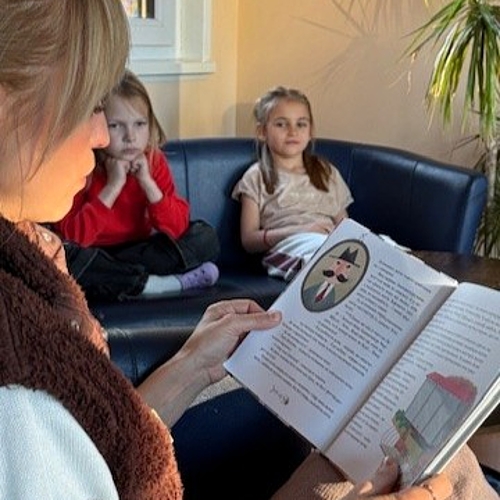 Iryna liest zwei Kindern auf Ukrainisch vor, die auf einem Sofa sitzen und gespannt zuhören.