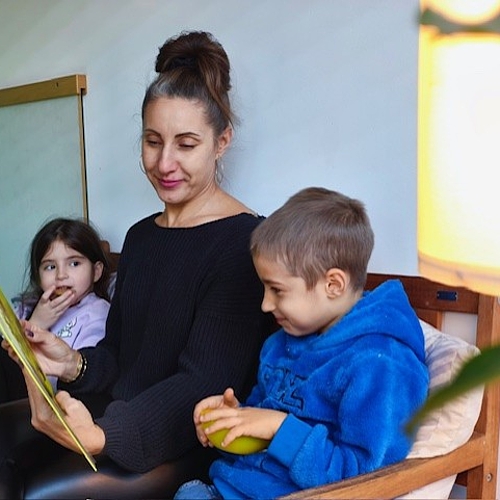 Eine Frau liest zwei Kindern auf Russisch vor. Die Kinder sitzen neben ihr und wirken interessiert.